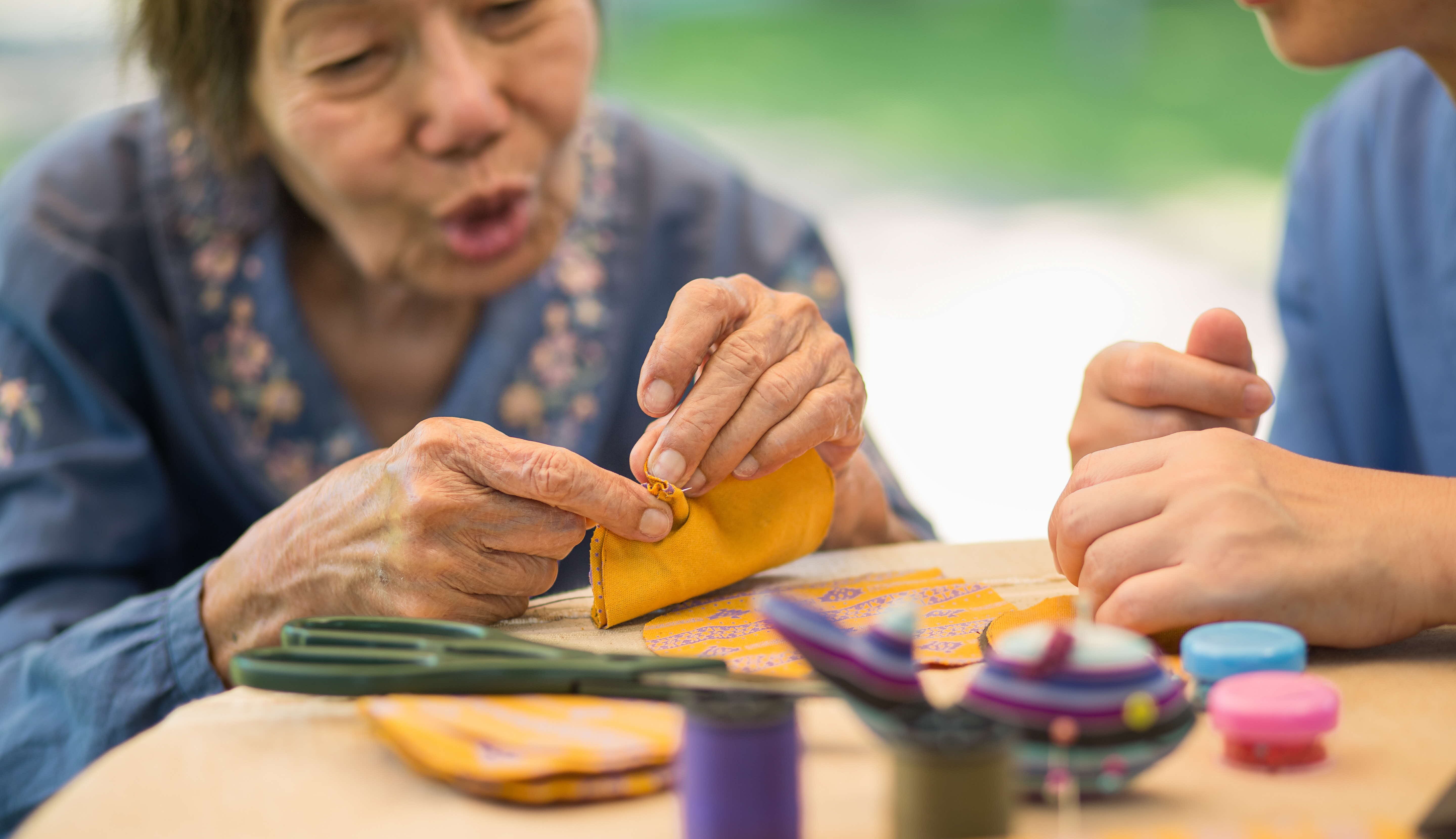 Elderly lady doing handicrafts with a caretaker